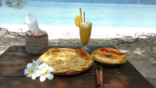 a table with two pizzas and a drink on a beach at Biru Meno Beach Bungalows in Gili Meno