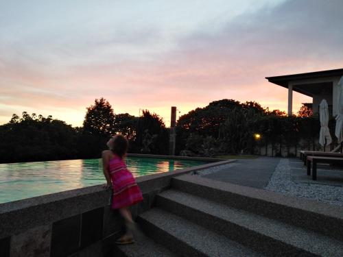 a woman walking by a pool at sunset at Ranis Lodge in Kampung Padang Masirat