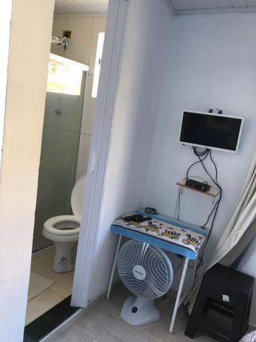 a bathroom with a toilet and a desk with a television at Kitnets da Tia Zeni in Arraial do Cabo