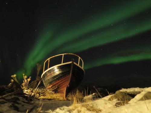 an old boat sitting on the shore under the aurora at Hlid Fisherman's Village in Álftanes