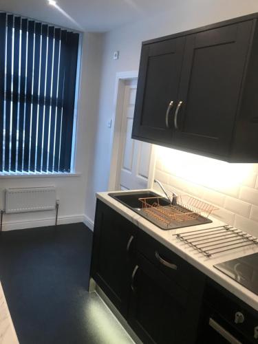 a kitchen with black cabinets and a sink and a window at Shores Holiday Apartments in Blackpool