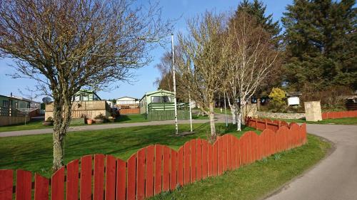 a red fence in front of a yard with trees at No42 Wild Goose in Dornoch