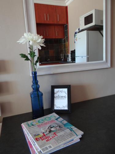 a table with a magazine and a blue vase with a flower at CREDO Guest House in Bloemfontein