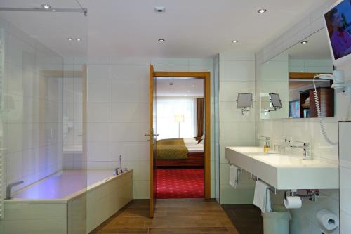a bathroom with a tub and two sinks and a mirror at Naturhotel Rügers Forstgut in Mespelbrunn