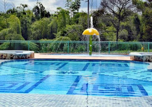 a swimming pool with an umbrella and a fountain at Hotel Campestre Paraiso Cafetero in Montenegro