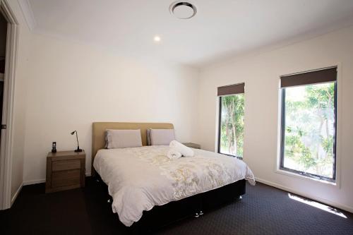 a white bedroom with a bed with a towel on it at THE BOARDWALK Relaxing Beachside Family Entertainer in Marcoola