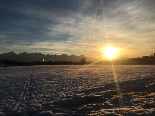 a sunset over a snow covered field with the sun in the sky at Haus Magnolia in Schwangau
