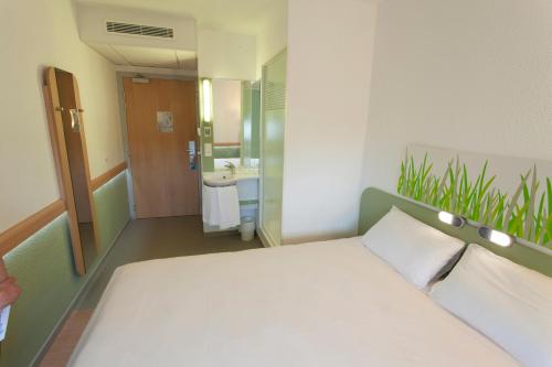a bedroom with a white bed and a bathroom at ibis budget Cherbourg - La Glacerie in Cherbourg en Cotentin