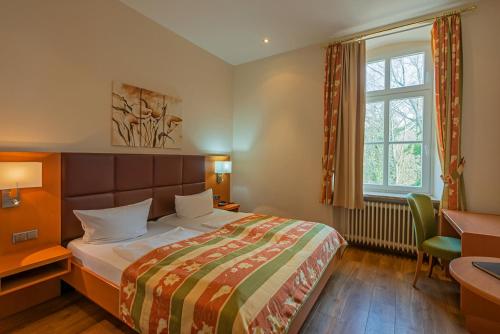 Schlafzimmer mit einem Bett, einem Schreibtisch und einem Fenster in der Unterkunft Berghotel Kockelsberg in Trier