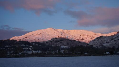 a mountain covered in snow next to a body of water at Bluebird Lodge in Coniston