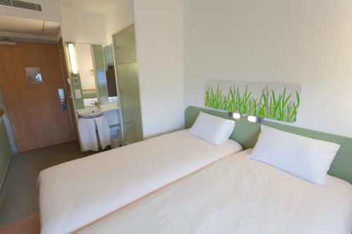 a large white bed in a room with a bathroom at ibis budget Cherbourg - La Glacerie in Cherbourg en Cotentin