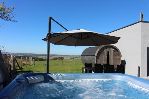 a hot tub with an umbrella next to a house at Eifel Dream Schneifelhaus in Kobscheid