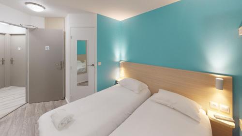 a bedroom with two beds and a blue wall at Hôtel du stade ex Kyriad Direct Lille Est Stade Pierre Mauroy in Villeneuve d'Ascq