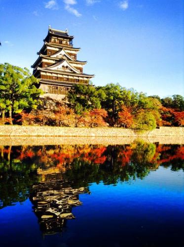 a building with a reflection in a body of water at Guesthouse POPTONE in Hiroshima