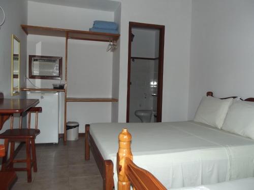 a bedroom with a bed and a table and a kitchen at Pousada Flats Paguru in Búzios