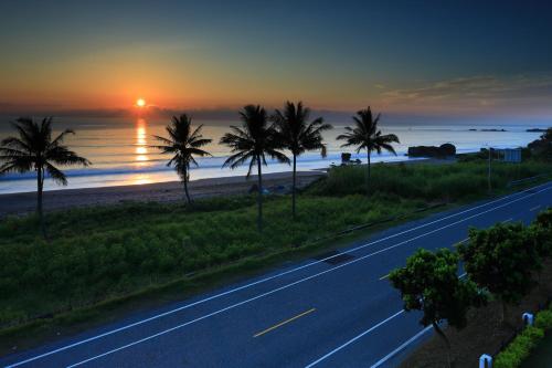 a road with palm trees and the ocean at sunset at Ji Li Ya Lan Homestay in Chenggong