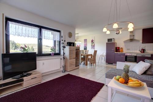 ein Wohnzimmer mit einem Sofa, einem TV und einem Tisch in der Unterkunft Ferienwohnung Seeblick in Schalkenmehren