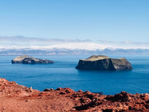 two islands in the water with mountains in the background at Guesthouse Árný in Vestmannaeyjar