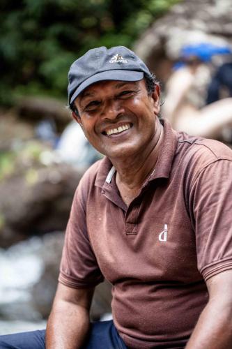a man wearing a hat sitting down smiling at Eco Villa - Sinharaja in Deniyaya