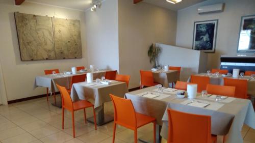 uma sala de jantar com mesas brancas e cadeiras laranja em ALBERGO METAURO em Fano