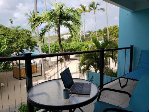 a laptop on a table on a balcony with palm trees at Secret Harbour Beach Resort in St Thomas