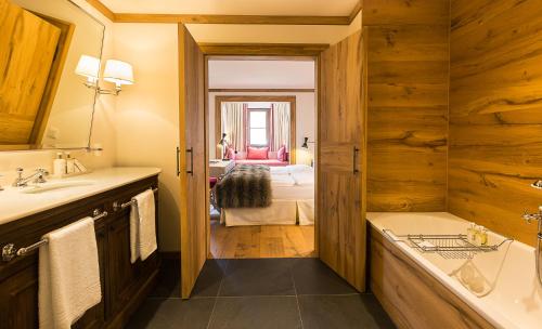 een badkamer met een wastafel en een bad en een slaapkamer bij House of Hütter - Wachtelhof Hotel & Spa in Maria Alm am Steinernen Meer