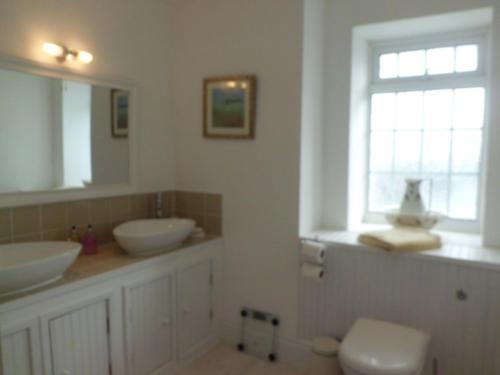 Un baño con dos lavabos y un inodoro y una ventana. en The Chantry, en Callington