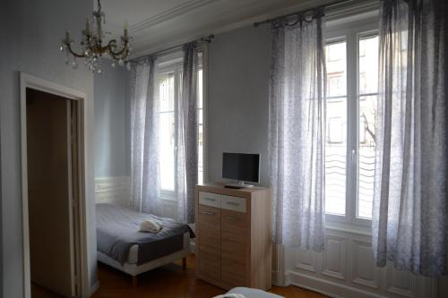 ein Schlafzimmer mit einem Bett und einem TV auf einer Kommode mit Fenstern in der Unterkunft Le cosy de la gare in Colmar