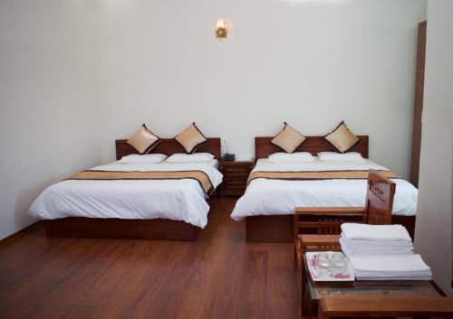 twee bedden in een kamer met houten vloeren en witte muren bij Hotel Nguyên Phước in Pleiku