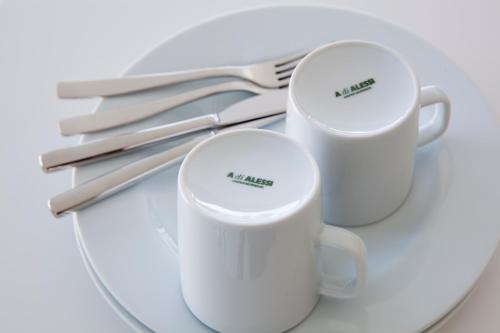 two white coffee mugs on a plate with silverware at Urban Residences Rotterdam in Rotterdam