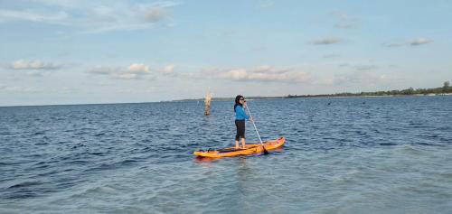 a woman standing on an orange paddle board in the water at Rock and Wreck Dive Resort in Tanjungbinga