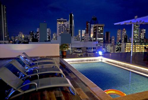 a rooftop pool with chairs and a city skyline at night at Victoria Hotel and Suites Panama in Panama City