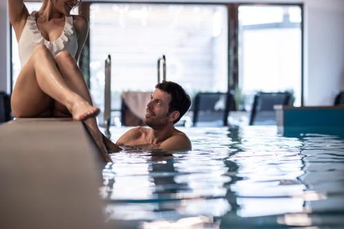 a man and a woman sitting in a swimming pool at Post Hotel - Tradition & Lifestyle Adults Only in San Candido