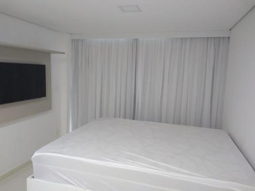 ein weißes Schlafzimmer mit einem Bett und einem Flachbild-TV in der Unterkunft Flat Centro de Porto de Galinhas Laguna Beach Flat in Porto De Galinhas