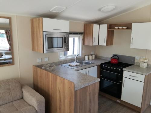 a small kitchen with a stove and a microwave at Private Caravan on Golden Sands Holiday Park, North Wales in Foryd