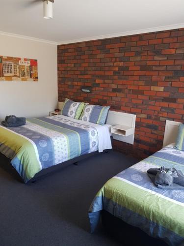 a bedroom with two beds and a brick wall at Coorrabin Motor Inn in Stawell