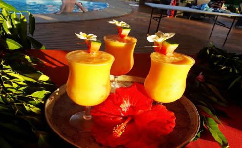 维拉港MG Cocomo Resort Vanuatu的盘子里摆放着四杯鸡尾酒，旁边放着一朵红花。