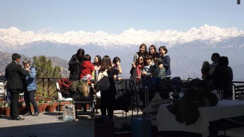 a group of people standing on a balcony with mountains in the background at Dhulikhel Mountain Resort in Dhulikhel