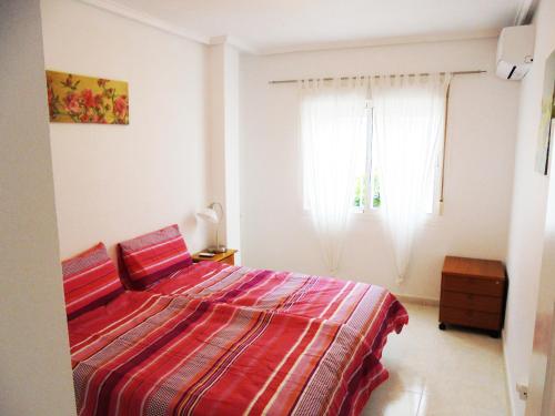 a bedroom with a bed with a red comforter and a window at Pancho Apartment Doña Pepa - C. Quesada in Rojales