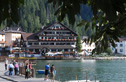 a group of people standing near the water in front of a building at Sporthotel Europa Sul Lago in Alleghe