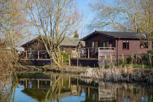 una cabaña de madera junto a un río con su reflejo en el agua en Fairwood Lakes Holiday Park en Westbury