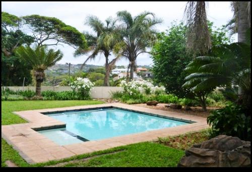einen Pool in einem Garten mit Palmen in der Unterkunft Mahogany Villa Guesthouse - SOLAR in Ballito