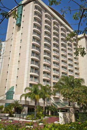a large white building with palm trees in front of it at Bourbon Residence Barra da Tijuca - Rio de Janeiro in Rio de Janeiro