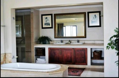 ein Badezimmer mit einer Badewanne, einem Waschbecken und einem Spiegel in der Unterkunft Mahogany Villa Guesthouse - SOLAR in Ballito