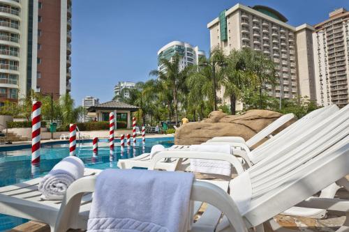 a group of white lounge chairs next to a swimming pool at Bourbon Residence Barra da Tijuca - Rio de Janeiro in Rio de Janeiro