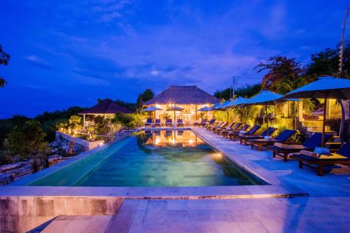 a resort pool with chairs and umbrellas at night at Bukit Taman Cottages in Nusa Lembongan