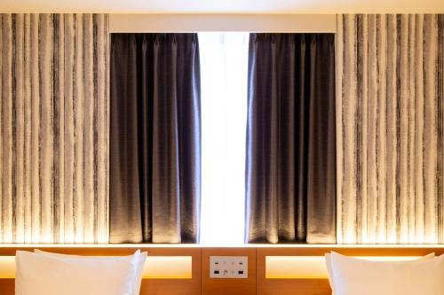a bedroom with a window with black curtains and white pillows at karaksa hotel grande Shin-Osaka Tower in Osaka