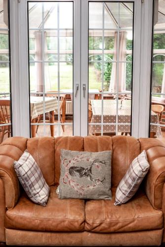 a brown leather couch with pillows in a living room at Trivelles Waterhall Country Gatwick Hotel & airport parking in Crawley