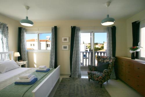 a bedroom with a bed and a chair and windows at Villa Carmel in Ayia Napa