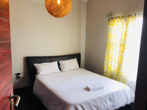 a bedroom with a white bed with a yellow curtain at Villa 134 Modipane in Gaborone